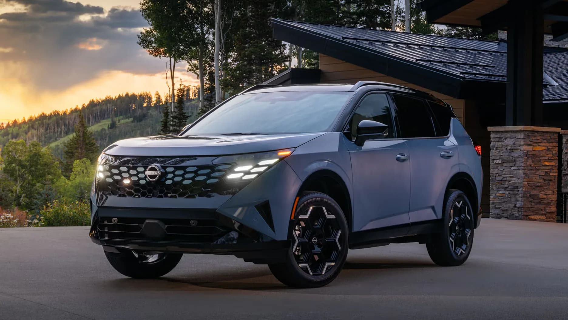 A modern Nissan SUV parked in front of a contemporary house at sunset, surrounded by trees and mountains.