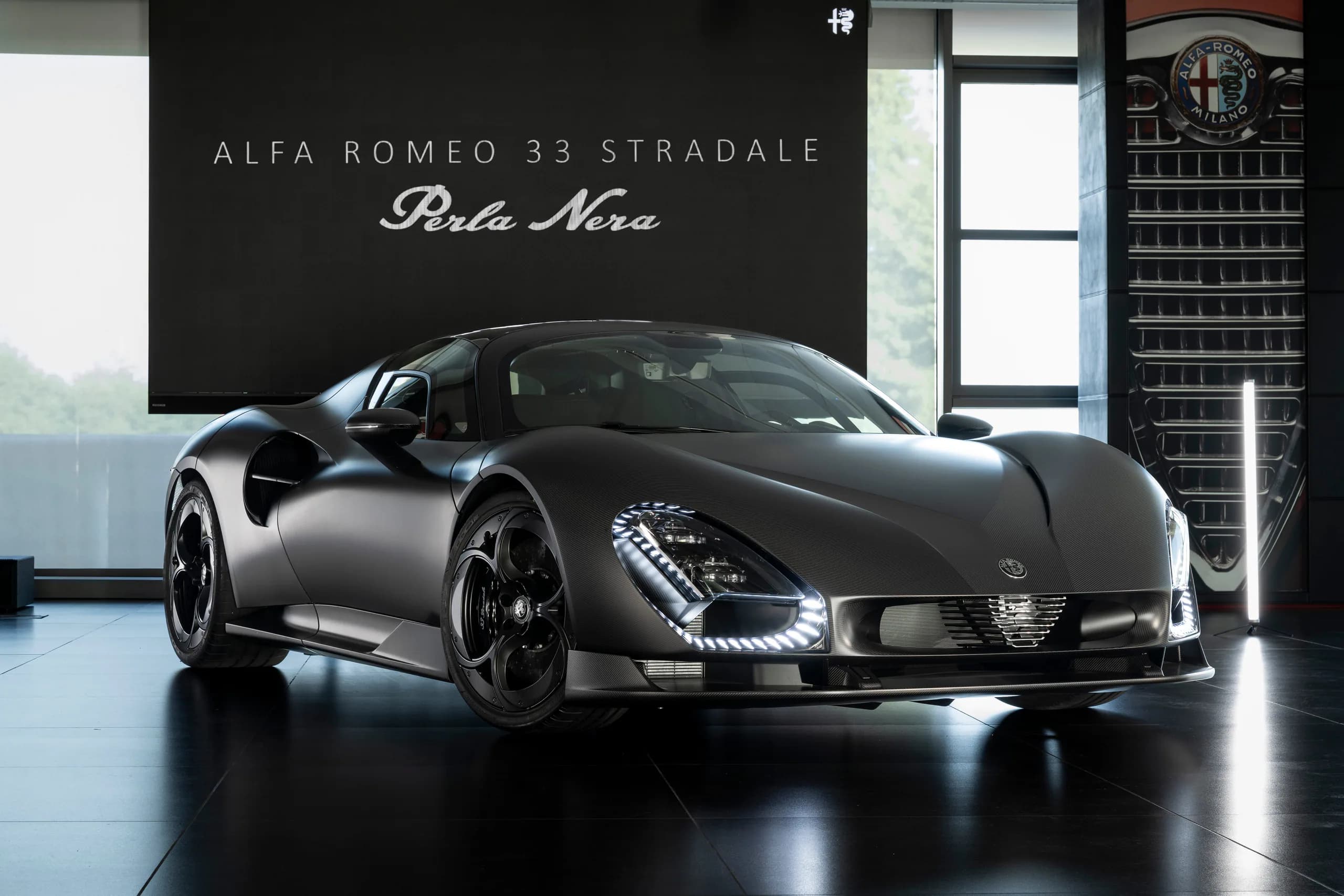Alfa Romeo 33 Stradale Perla Nera in a modern showroom setting with sleek design and dramatic lighting.